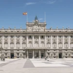 a large building with columns and a flag on top with Royal Palace of Madrid in the background